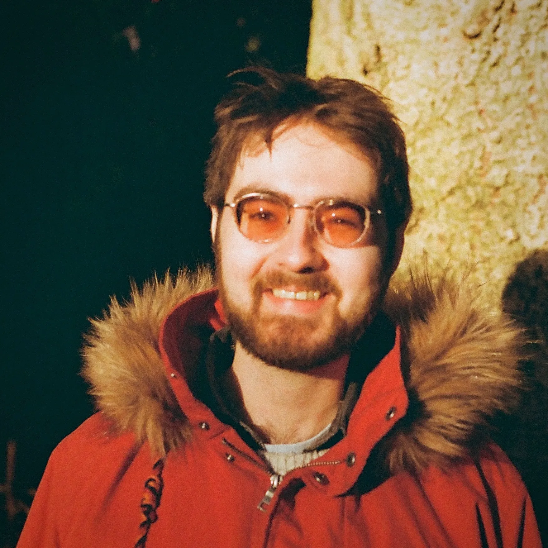 A photo of Jay Pocknell. He has short brown hair and a beard. He is wearing tinted glasses and a red parka with a fur lined…