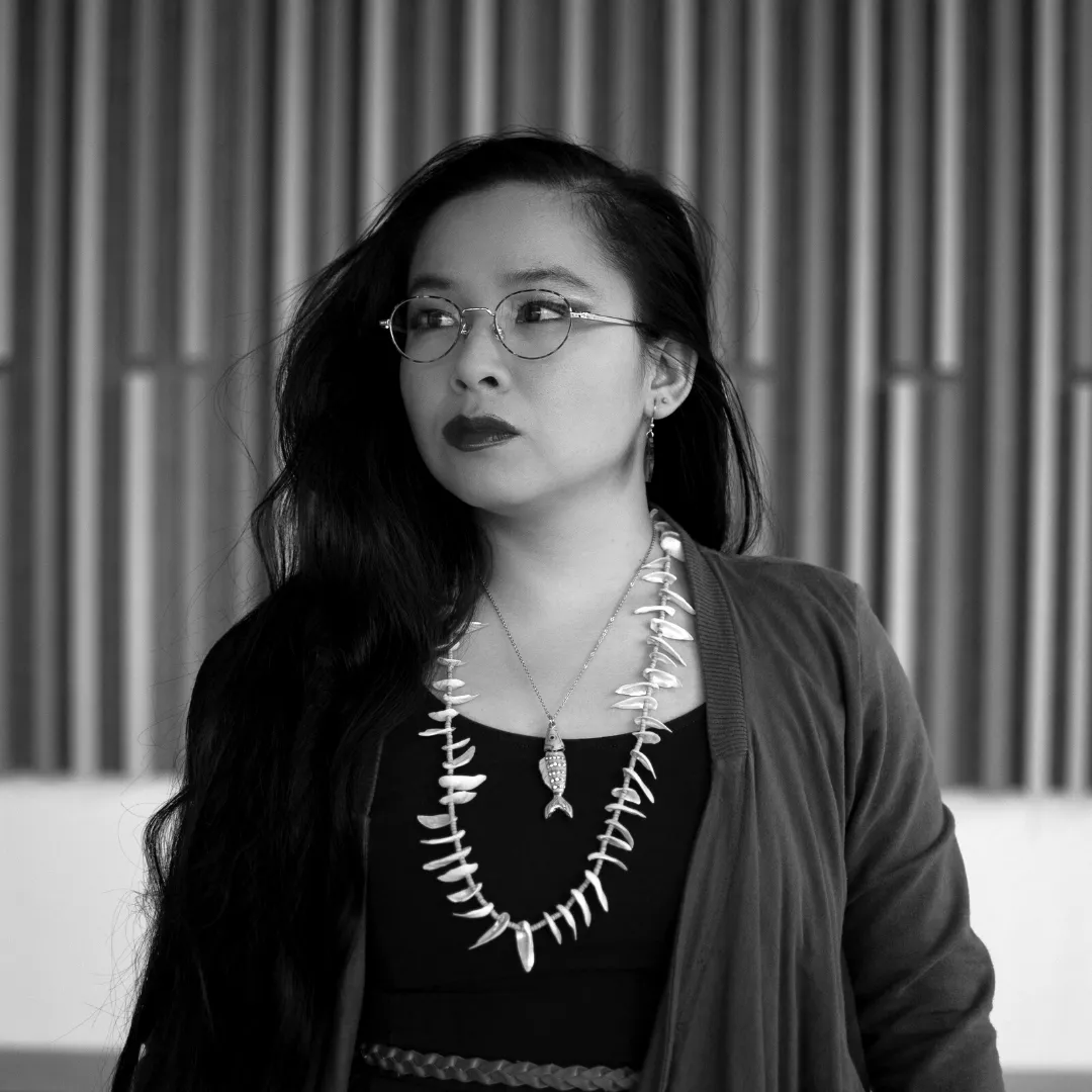 Black and white headshot of a Vietnamese woman, King Kimbit, who has long, dark hair, and is wearing a long necklace…
