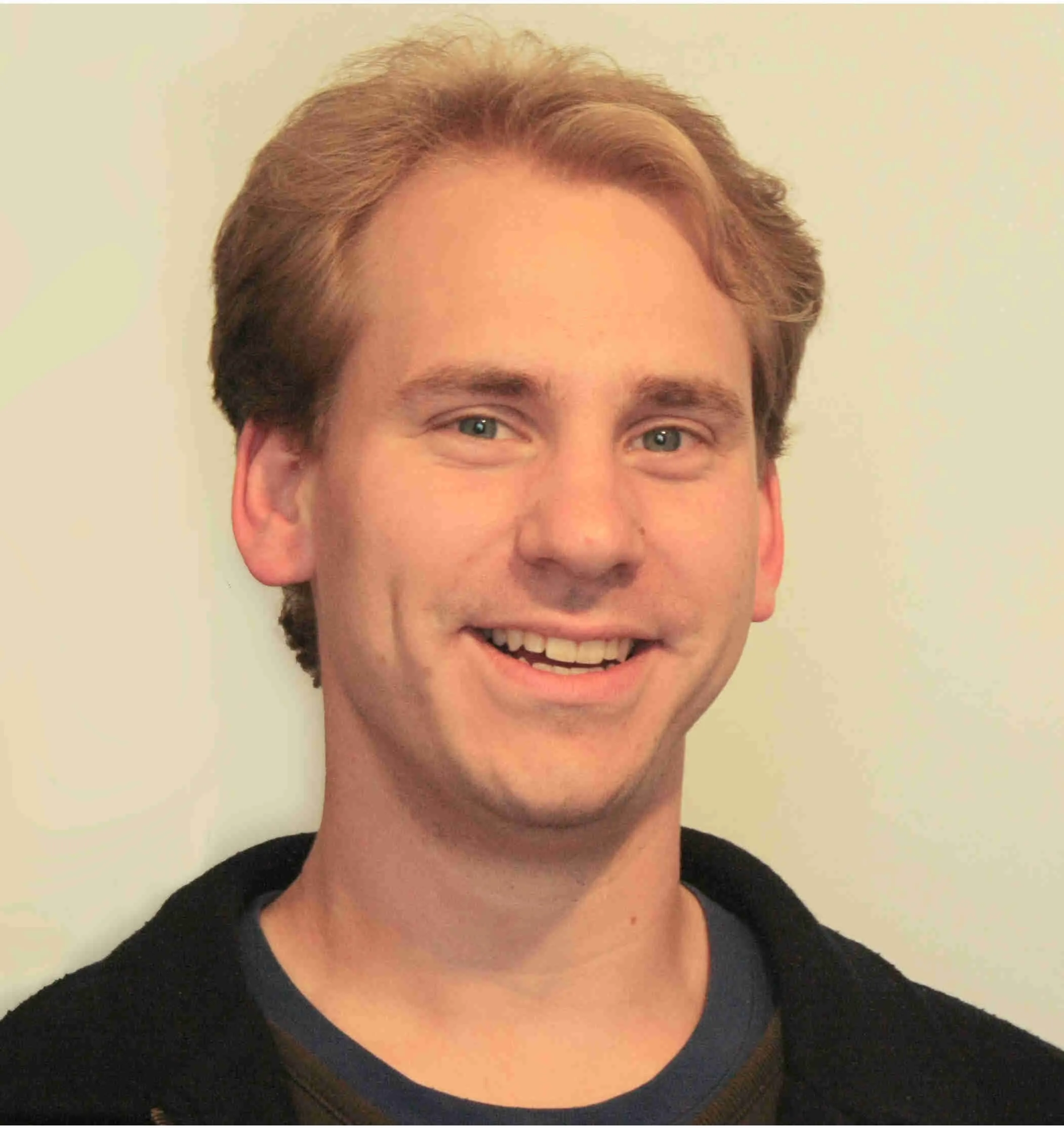 Headshot of Colin Tucker, a white man with short brown hair, wearing a black t-shirt. He is smiling at the camera